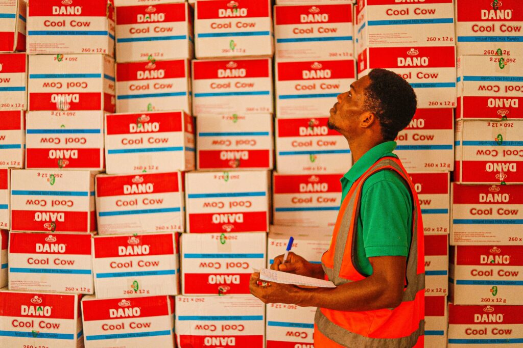pexels-photo-8069551-8069551 A warehouse worker examining stacked boxes labeled 'Dano Cool Cow'.